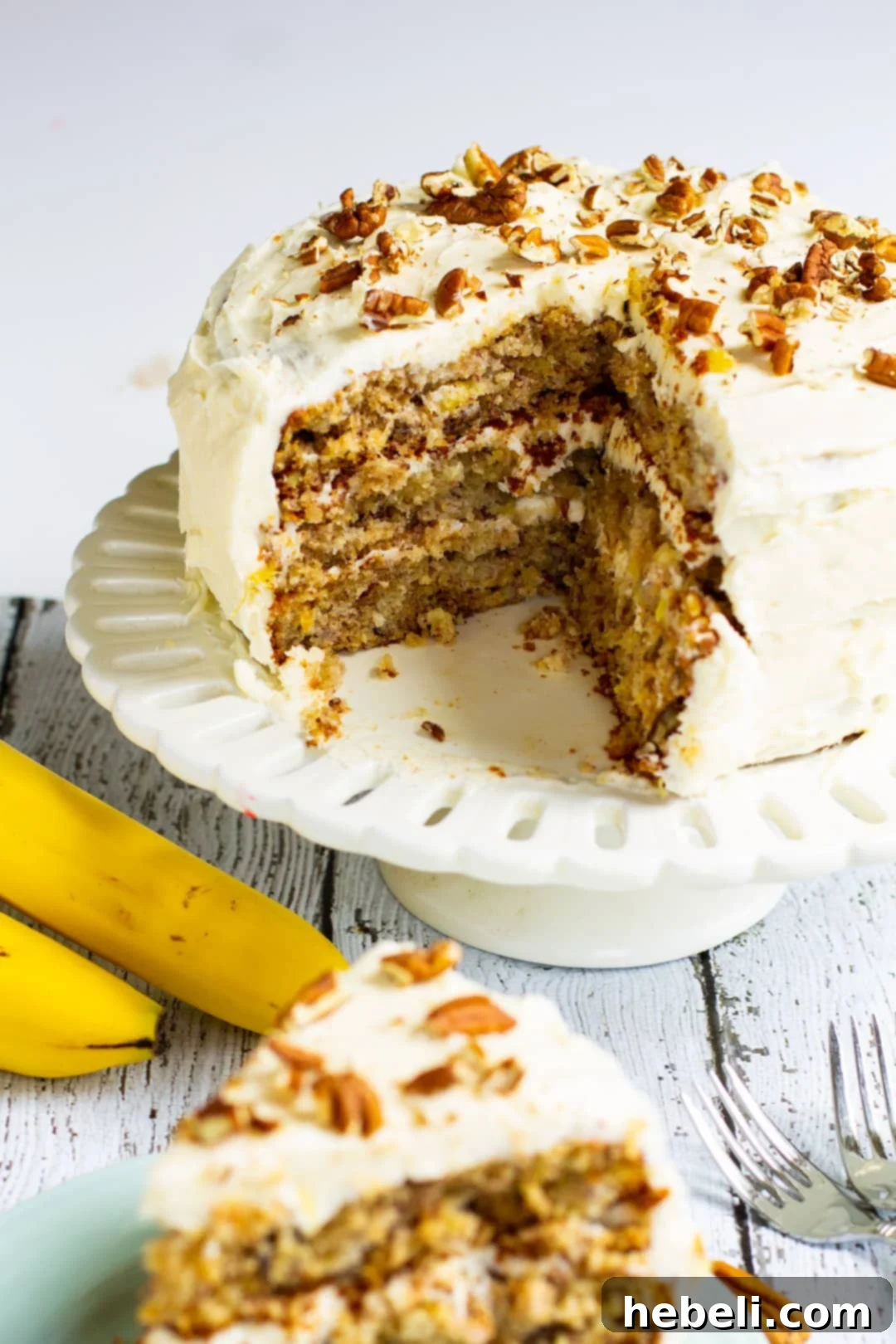 Banana Pineapple Pecan Paradise 3 A stunning three-layer Hummingbird Cake, fully frosted with cream cheese icing and topped with toasted pecans, resting on a cake stand.