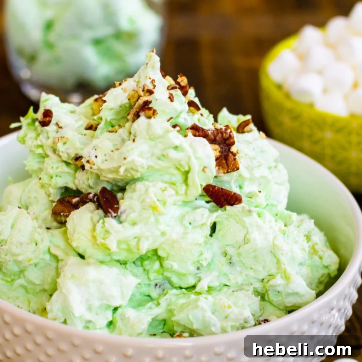 A large glass bowl filled with vibrant green Watergate Salad, generously topped with chopped pecans, ready to be served at a gathering.