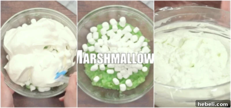 A close-up image showing a person gently folding creamy whipped topping and miniature marshmallows into the light green pistachio and pineapple mixture in a large bowl.