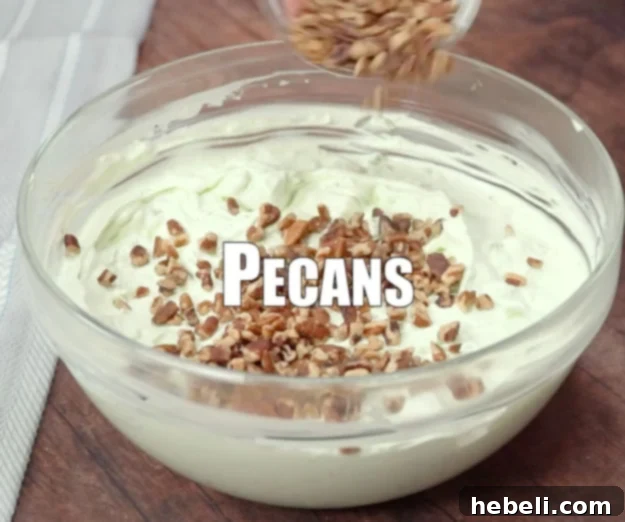 A hand sprinkling freshly chopped toasted pecans over the top of a bowl of chilled Watergate Salad, preparing it for serving.