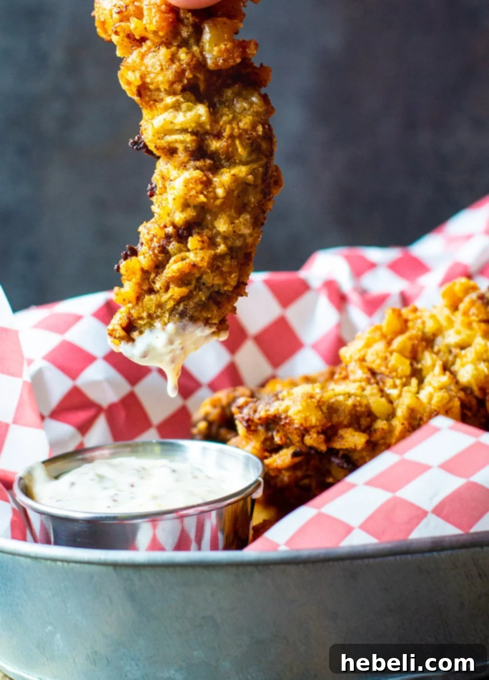 A Chicken Fried Steak Finger being dipped into a bowl of rich Creole Mustard Sauce, highlighting its crispy texture.