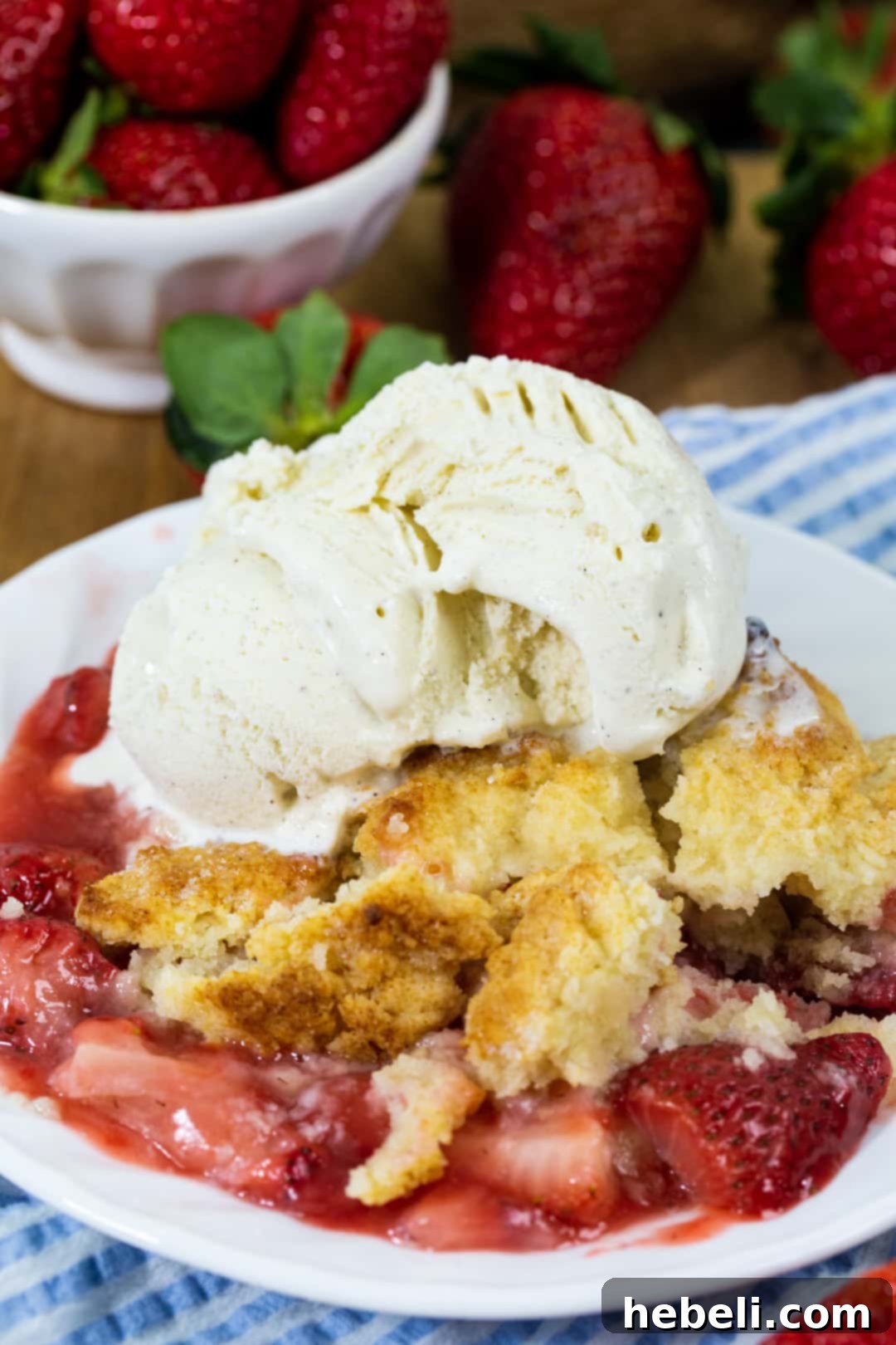 A serving of Strawberry Cobbler topped with melting vanilla ice cream on a white plate, ready to be eaten.