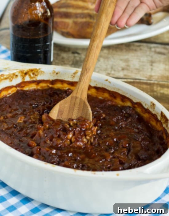 Sassafras Infused Baked Beans 3 Close-up shot of Root Beer Baked Beans simmering in a baking dish, with visible bacon bits.