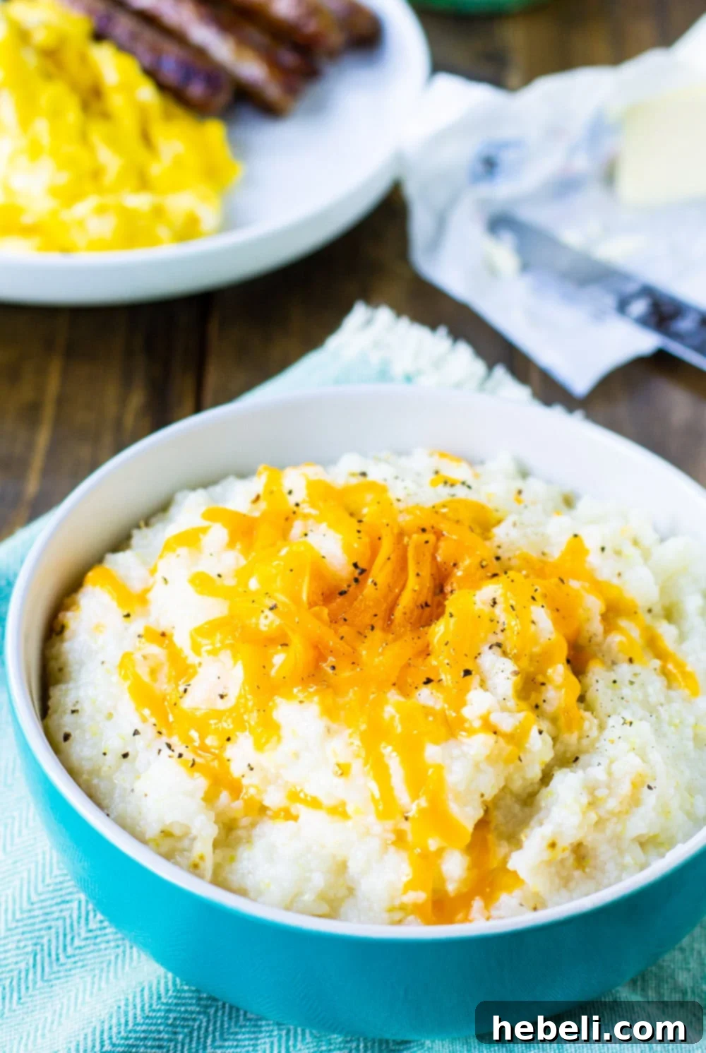 A delicious bowl of crockpot grits served with crispy bacon and fried eggs in the background, a perfect southern breakfast.