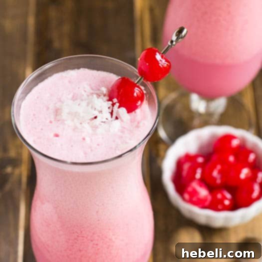 A glass of Pink Coconut Frost Cocktail garnished with a cherry