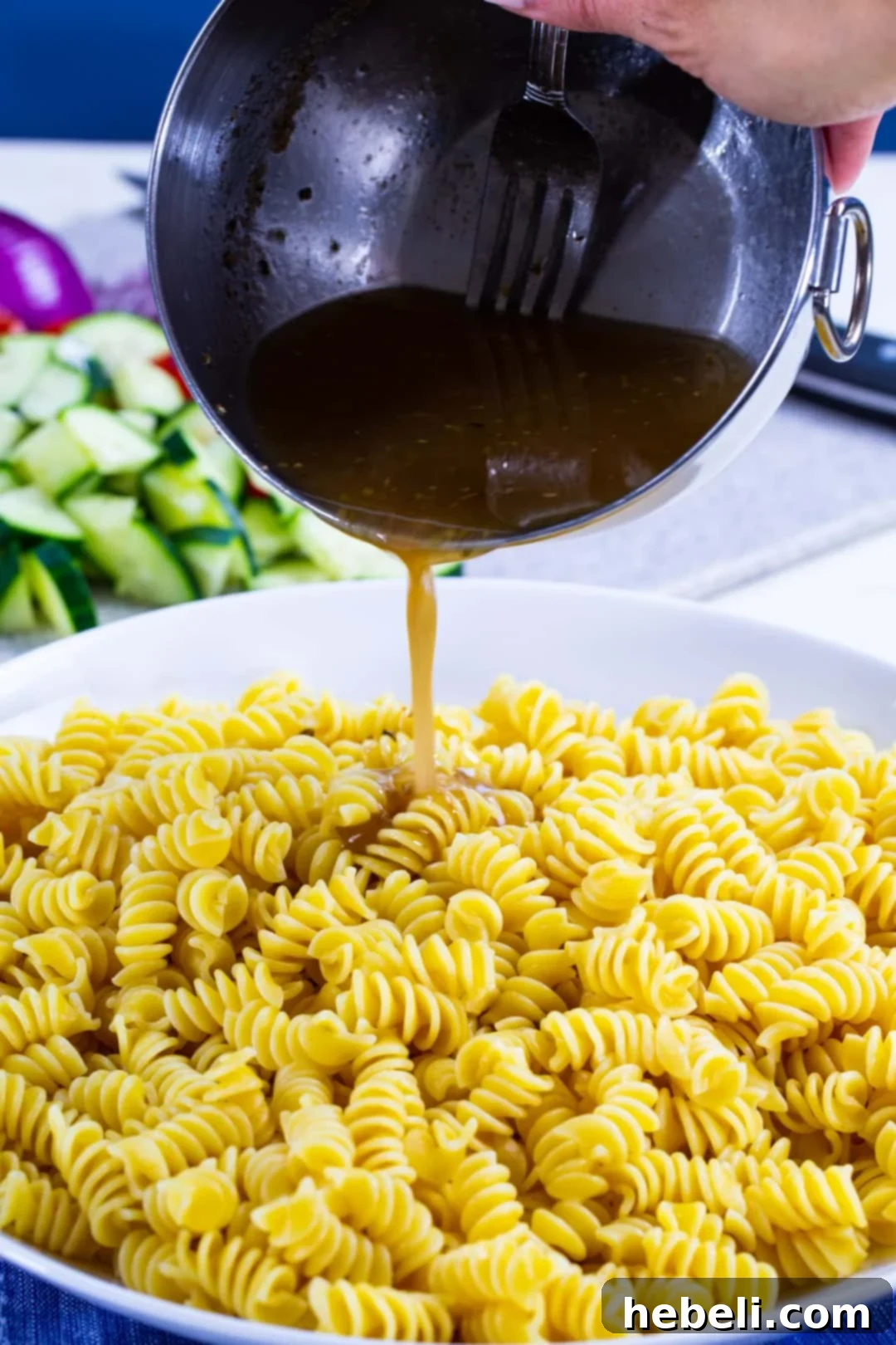 Zesty Greek Pasta Salad 3 Zesty homemade vinaigrette being poured over cooked pasta and fresh ingredients for Greek Pasta Salad.