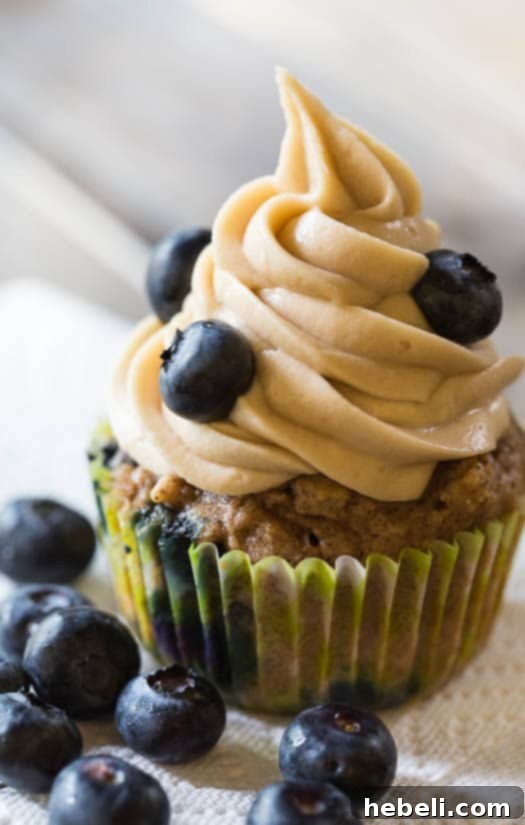 Luscious Blueberry Maple Cupcakes 5 Two beautifully frosted Blueberry Maple Cupcakes resting on a rustic wooden surface, highlighting their homemade charm