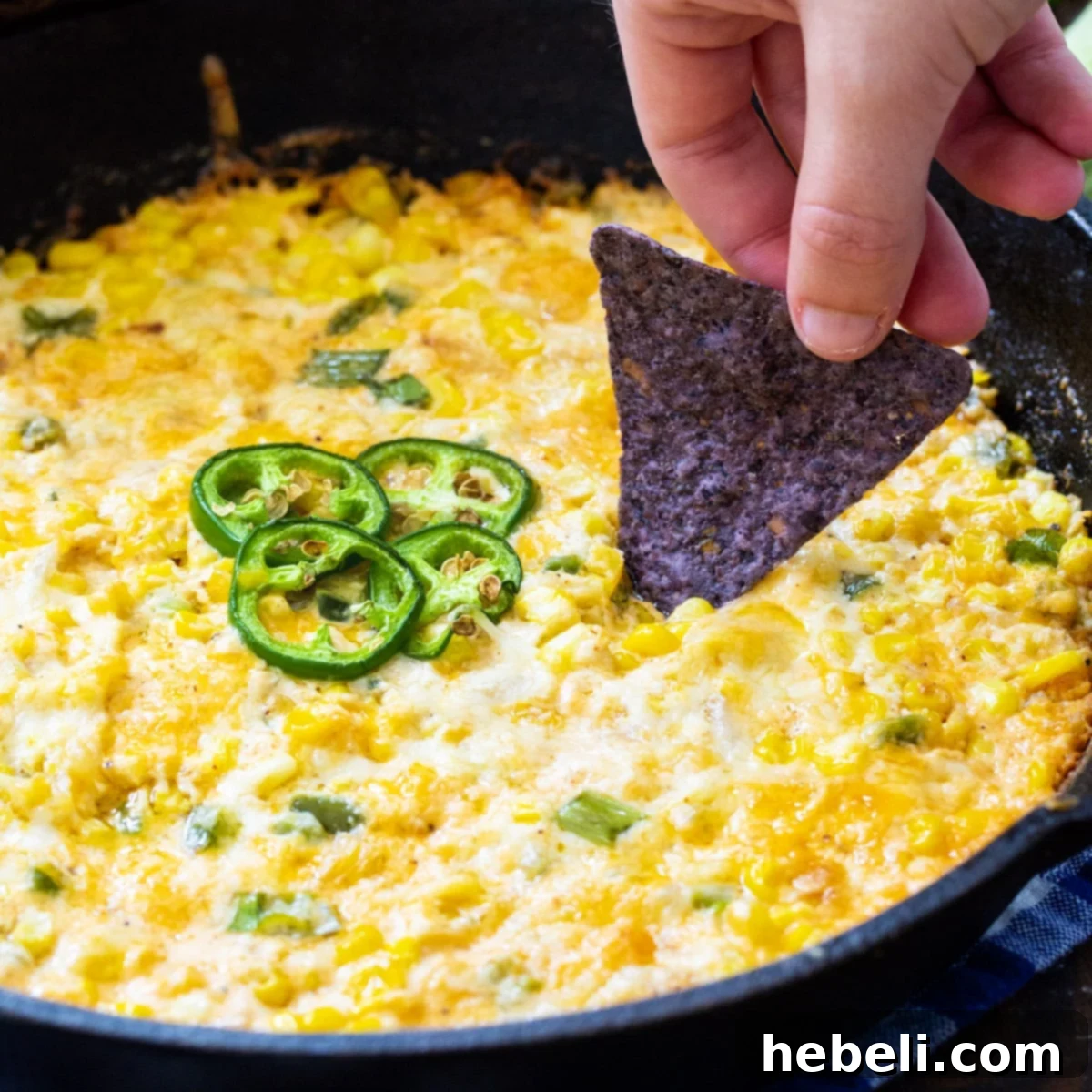 Scooping up Hot Corn Dip with Jalapeños with a tortilla chip, showcasing its creamy texture and melty cheese.