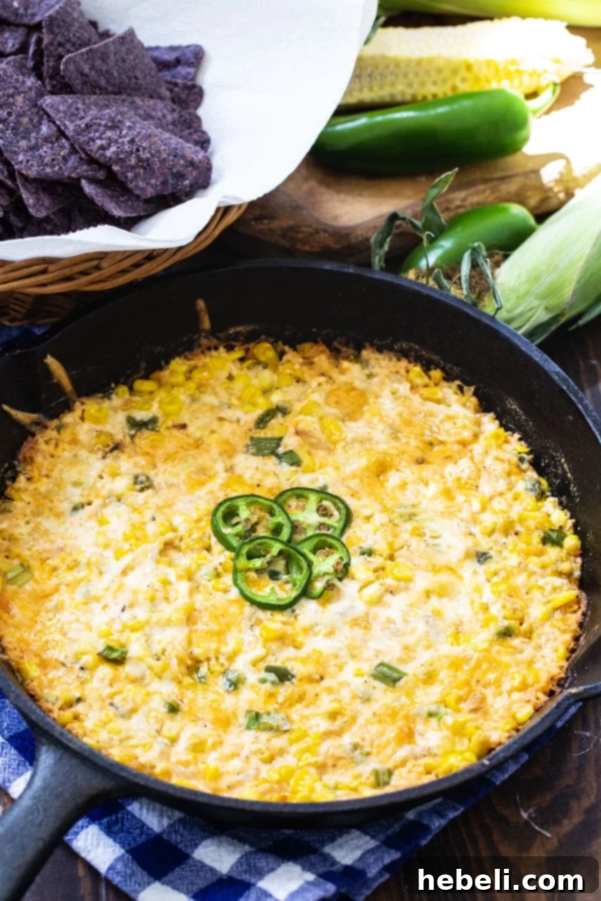 Hot Corn Dip with Jalapeños served in a rustic cast iron pan, surrounded by a pile of golden tortilla chips.