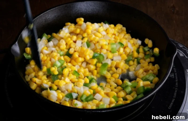 Close-up of corn, onion, and jalapeños being sautéed in butter in a skillet.