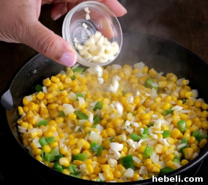 Adding minced garlic to the sautéed corn and jalapeño mixture in a skillet.