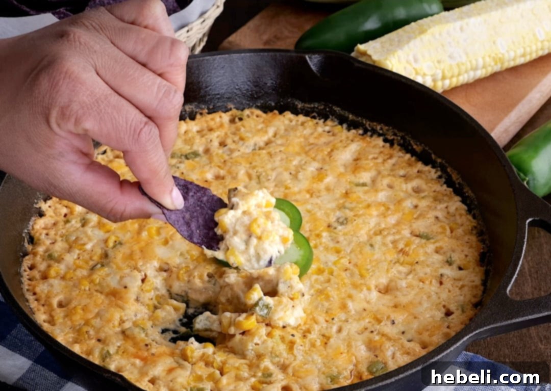 A tortilla chip being dipped into the hot, bubbly, and cheesy corn dip fresh from the oven.