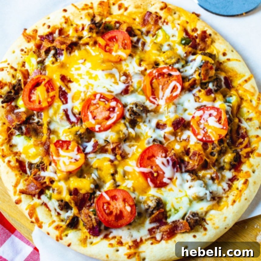 Overhead view of a freshly baked Cheeseburger Pizza, showcasing its generous toppings of ground beef, bacon, pickles, tomatoes, and melted cheese on a golden crust.