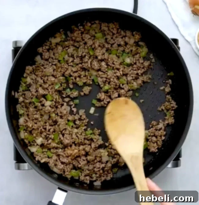 Ground beef, diced onions, and green peppers cooking in a skillet.