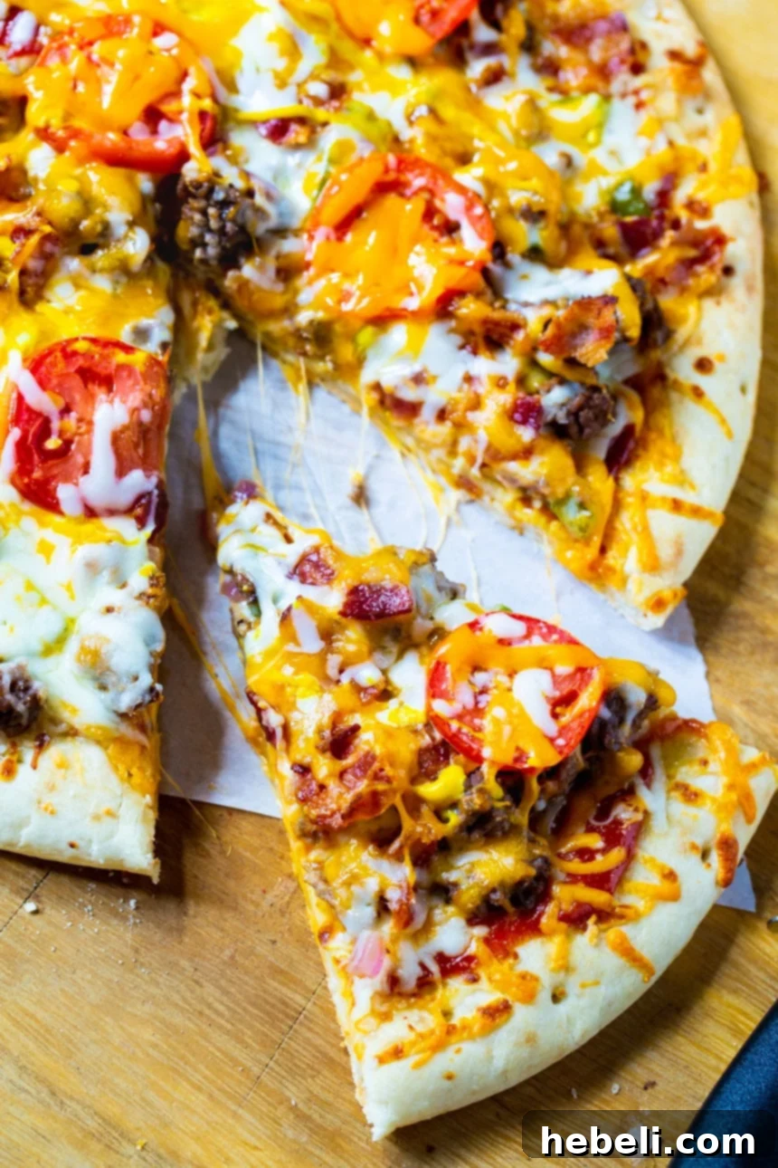 A large slice of Cheeseburger Pizza being lifted from the whole pizza, showing gooey cheese and toppings.