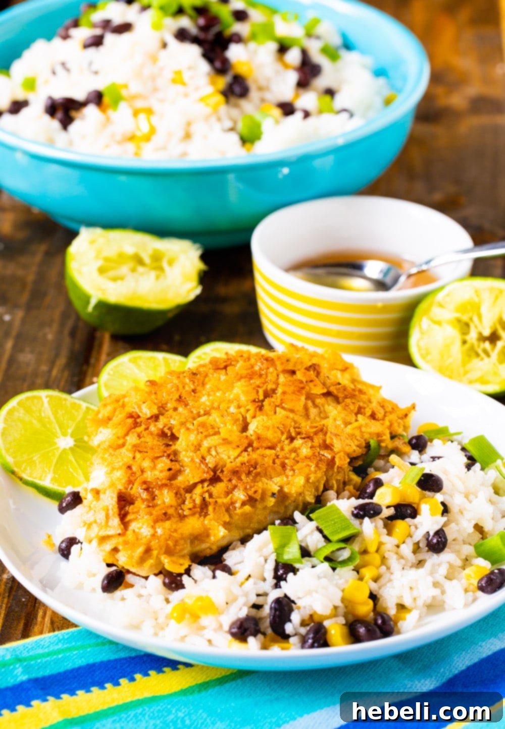 Close-up shot of Tortilla Crusted Chicken and Coconut Rice with black beans and corn on a plate, with a bowl of rice blurred in the background.