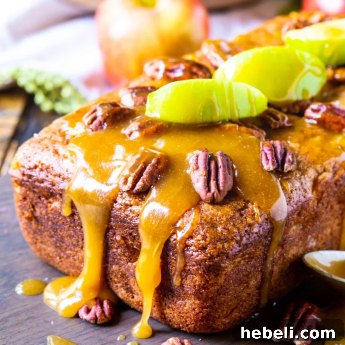 A beautifully baked loaf of Caramel Apple Bread, drizzled with sweet caramel glaze and topped with crunchy toasted pecans, with fresh apple slices nearby.