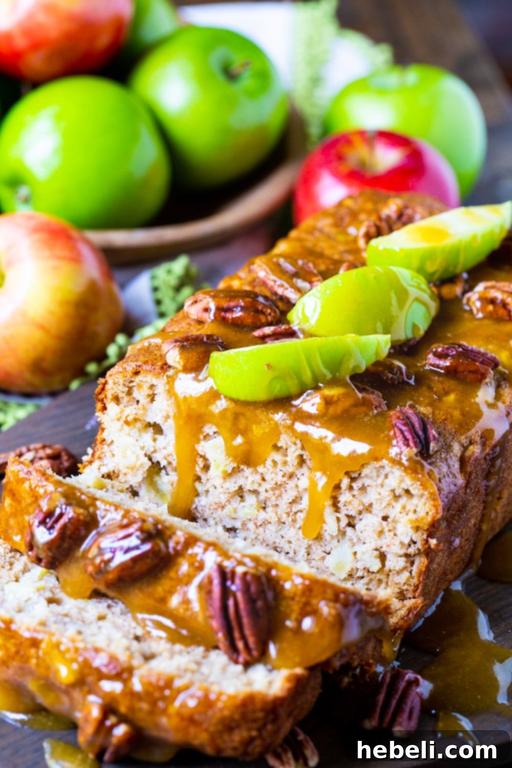 A loaf of Caramel Apple Bread with several slices already cut, revealing the moist interior studded with apple pieces, and a generous caramel glaze.