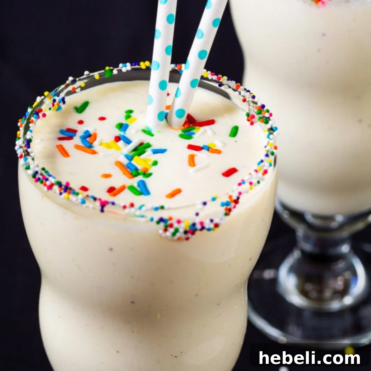 Two glasses of creamy Cake Batter Milkshakes topped with colorful sprinkles.