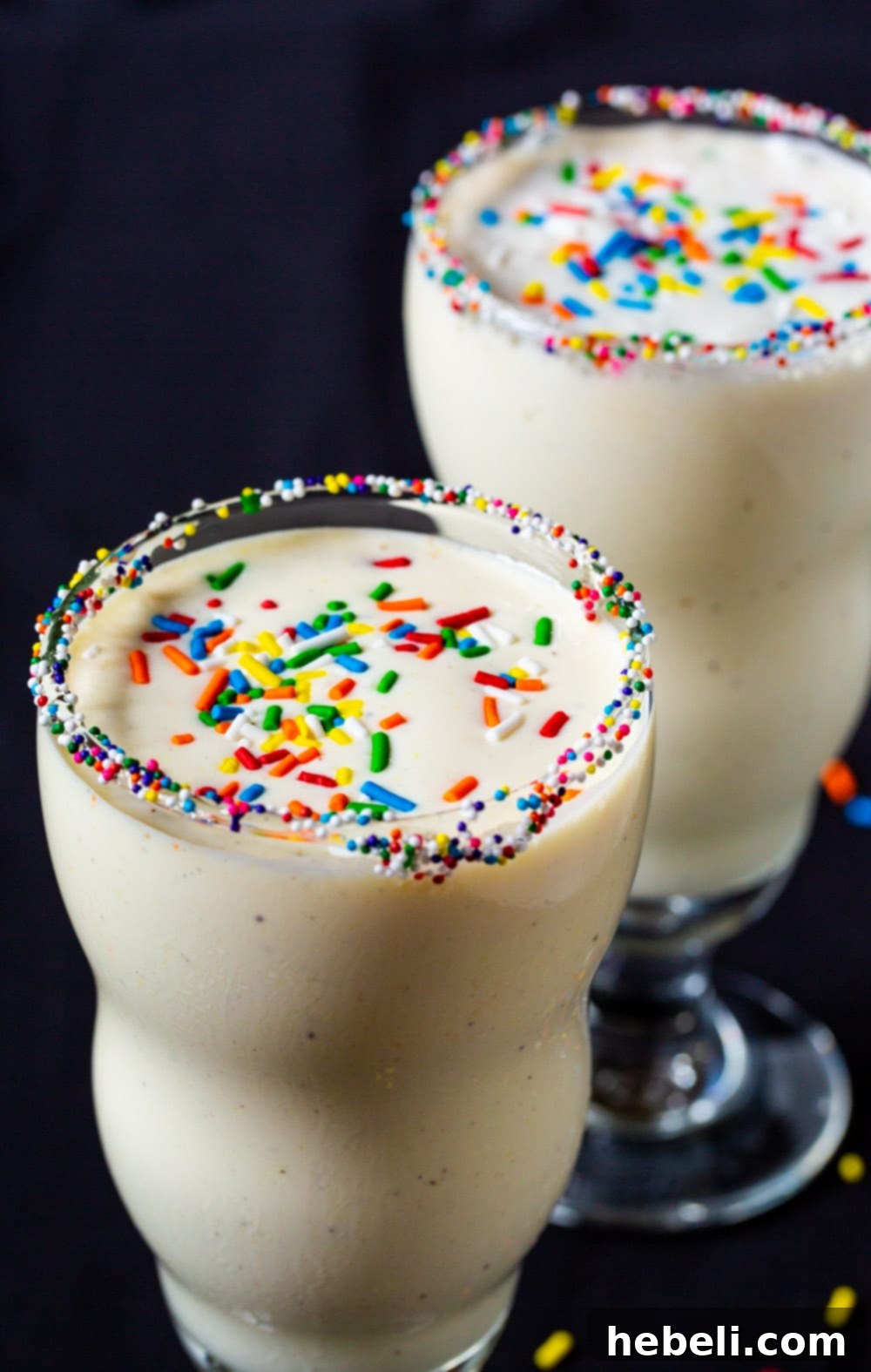 Creamy milkshakes in two glasses, generously topped with vibrant sprinkles.