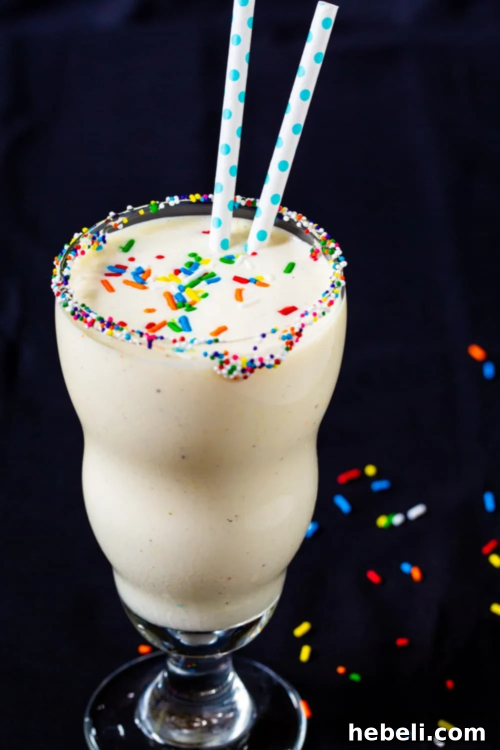 Close-up of a Cake Batter Milkshake in a glass with two straws, topped with sprinkles.