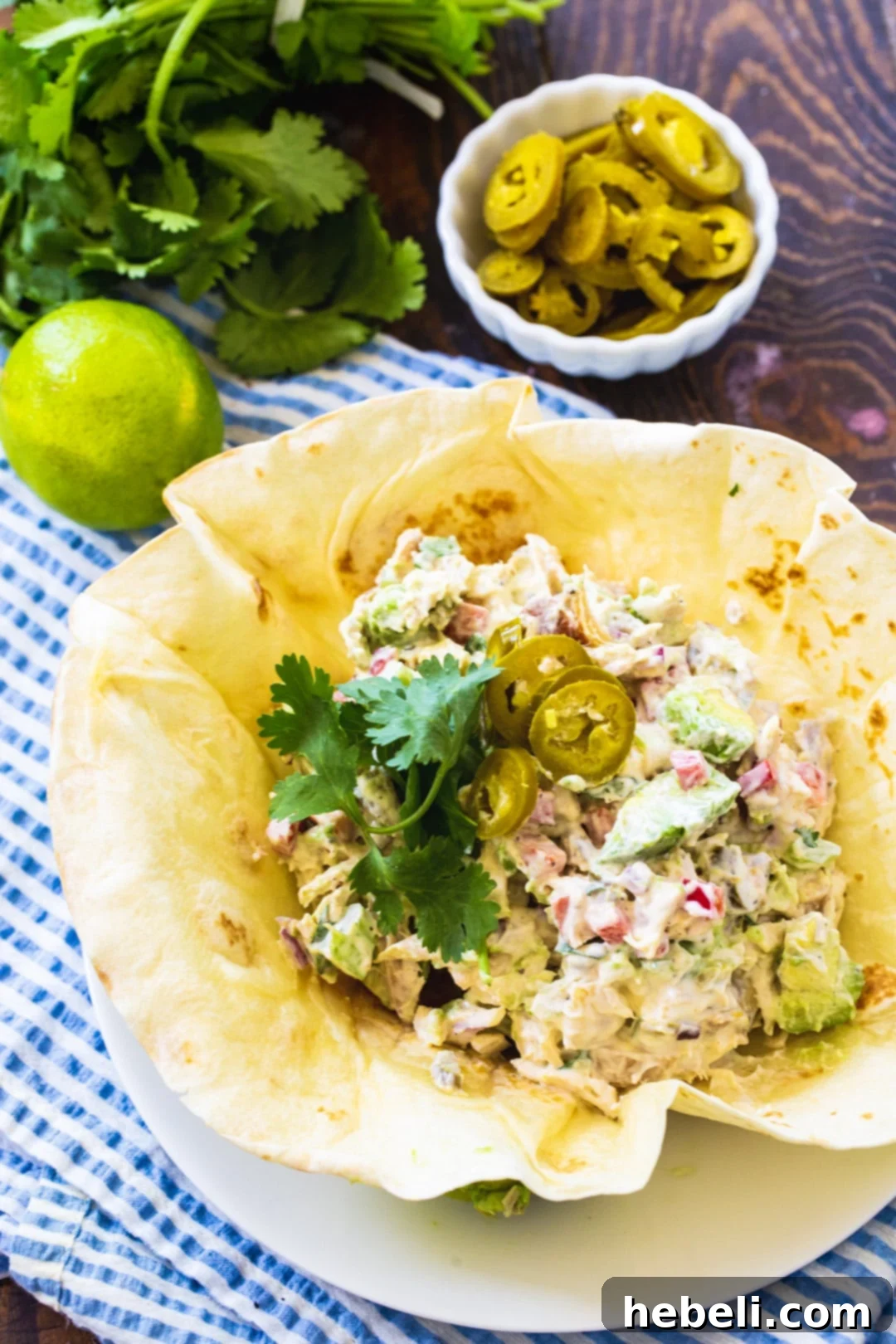 Bold Jalapeno Chicken Salad 3 Close-up of creamy Jalapeño Chicken Salad in a tortilla bowl, surrounded by fresh cilantro leaves and a small bowl of sliced pickled jalapeños, highlighting its fresh ingredients.