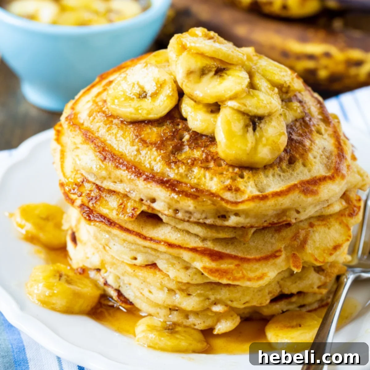 Stack of golden-brown Banana Pancakes generously drizzled with glistening Caramel-Banana Syrup, adorned with fresh banana slices on a white plate.
