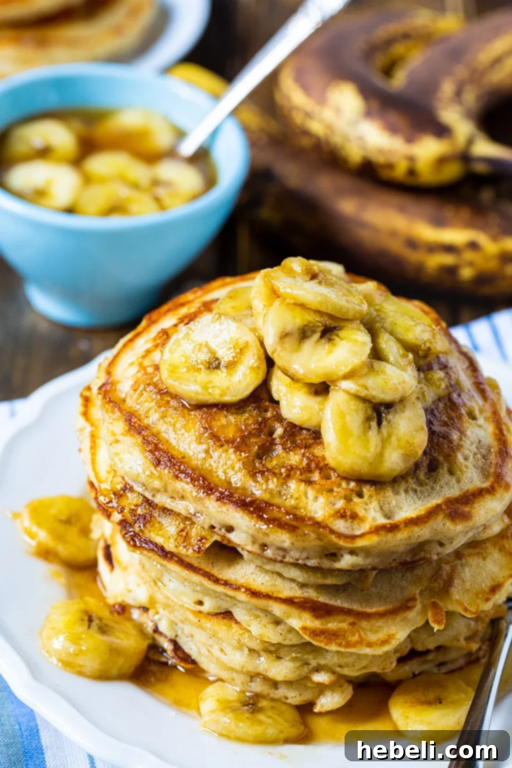Close-up of a stack of golden banana pancakes, topped with glistening caramel sauce and thinly sliced bananas, ready to be served.