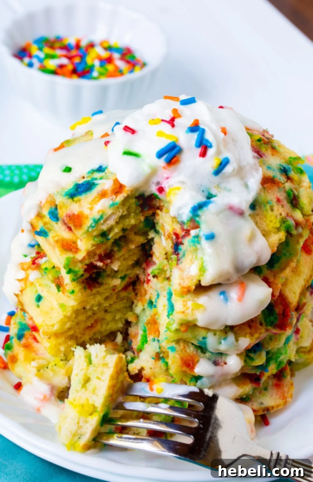 A fork holding a piece of golden-brown Cake Batter Pancake, topped with powdered sugar glaze and sprinkles, ready to be eaten.