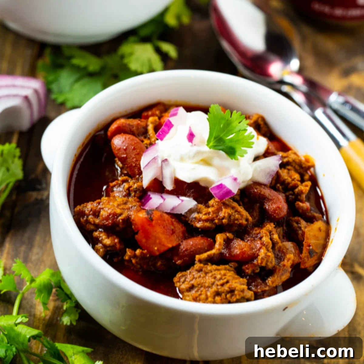 A vibrant bowl of Dr Pepper Chili, richly topped with cool sour cream and finely diced red onion, inviting diners to indulge.
