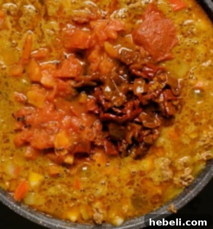 Worcestershire sauce being poured into the chili mixture in a Dutch oven.