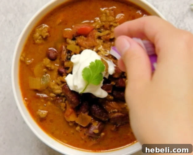 A bowl of Dr Pepper Chili being topped with fresh cilantro and red onion slices.