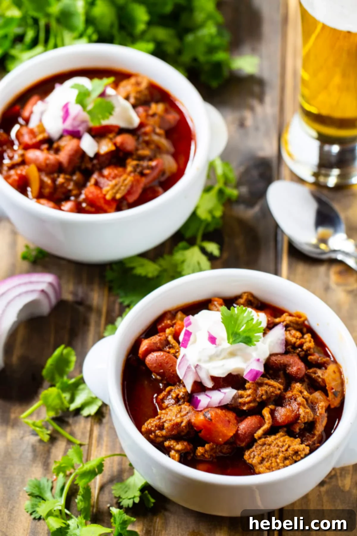 Two bowls of Dr Pepper Chili presented alongside a refreshing glass of beer, highlighting a perfect meal pairing.