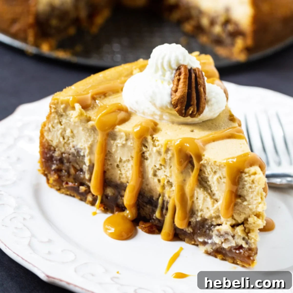A beautifully presented slice of Pecan Pie Cheesecake, generously topped with fluffy whipped cream and a luscious caramel sauce drizzle.