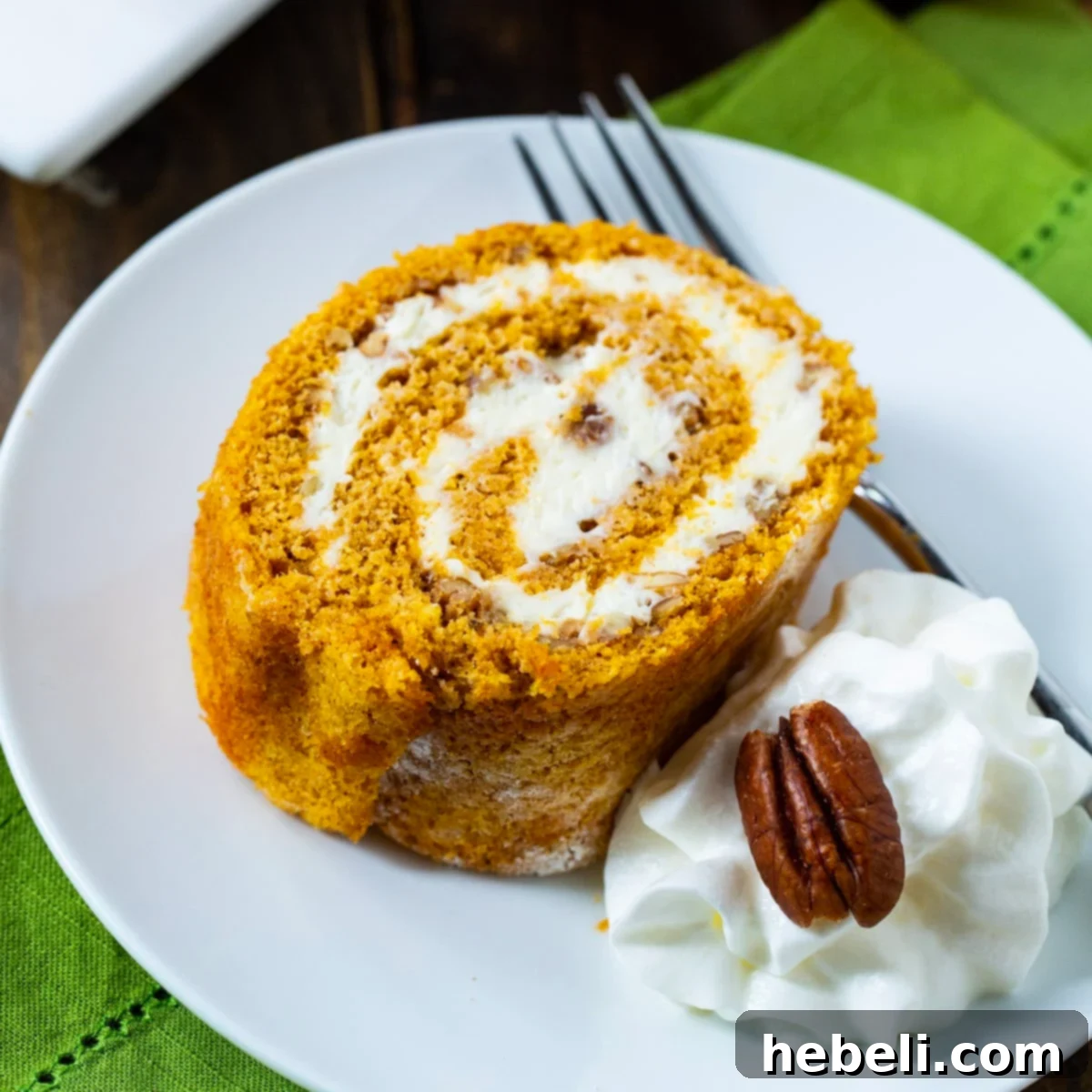 A perfectly sliced Pumpkin Cake Roll on a plate, garnished with a dollop of whipped cream, showcasing its beautiful spiral.