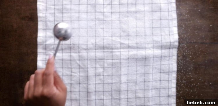 Sprinkling a generous amount of powdered sugar onto a clean, flat kitchen towel, preparing for the warm cake.