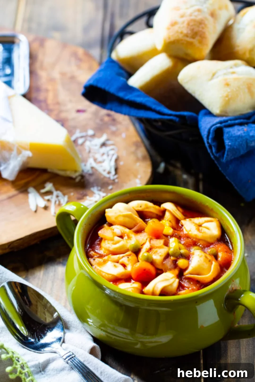 Easy Tortellini Soup in a rustic bowl with crusty bread rolls in a basket beside it.
