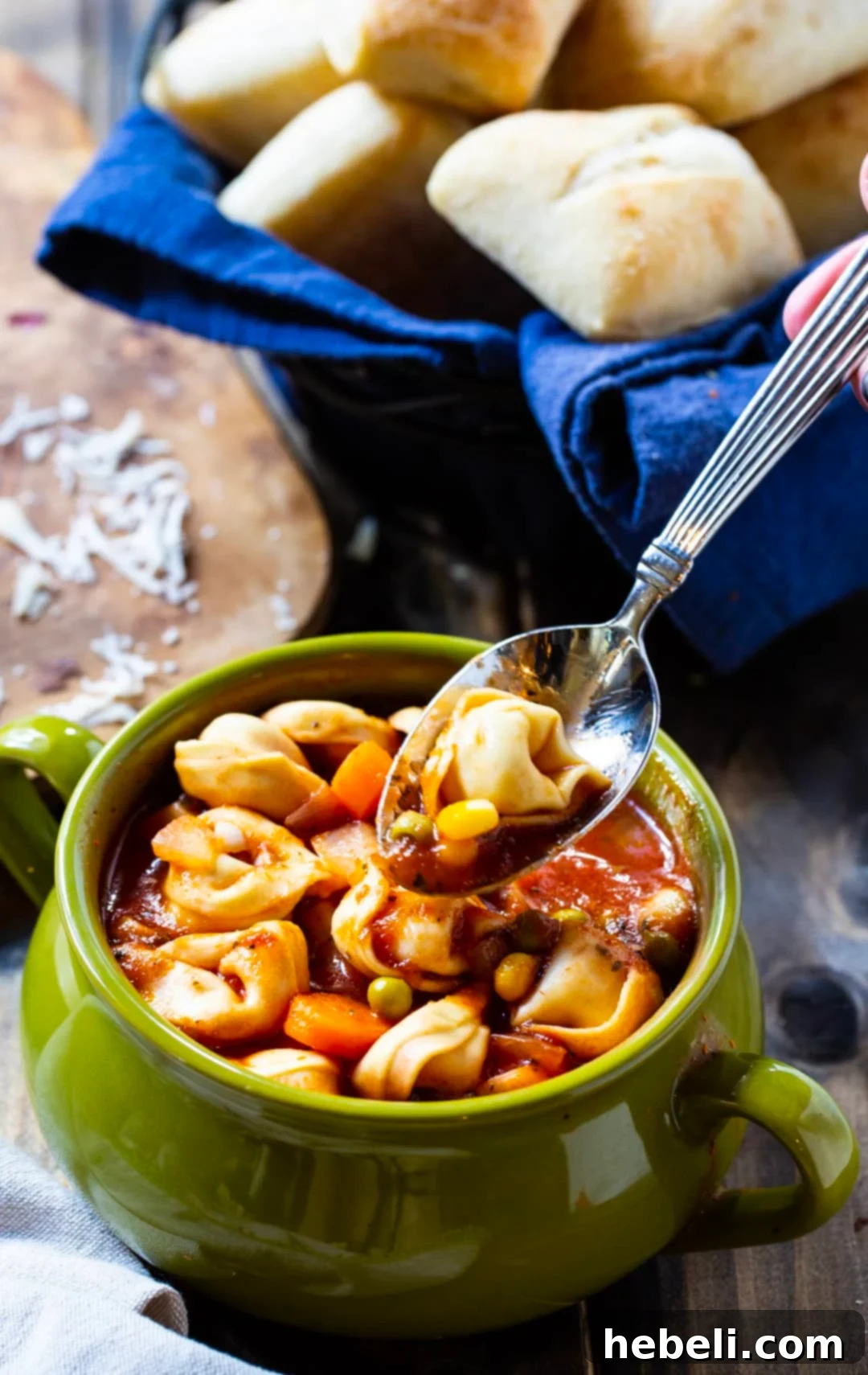 A spoon diving into a bowl of rich tortellini soup, highlighting the textures and ingredients.
