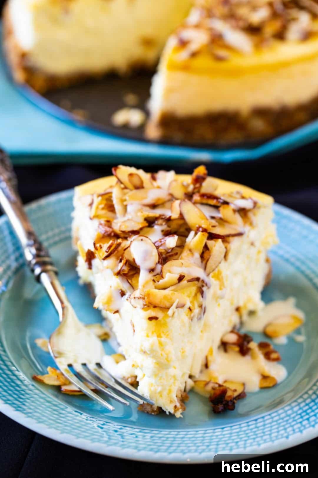A close-up shot of a slice of Amaretto Cheesecake on a vibrant blue plate, highlighting the sugared almond topping and creamy filling.