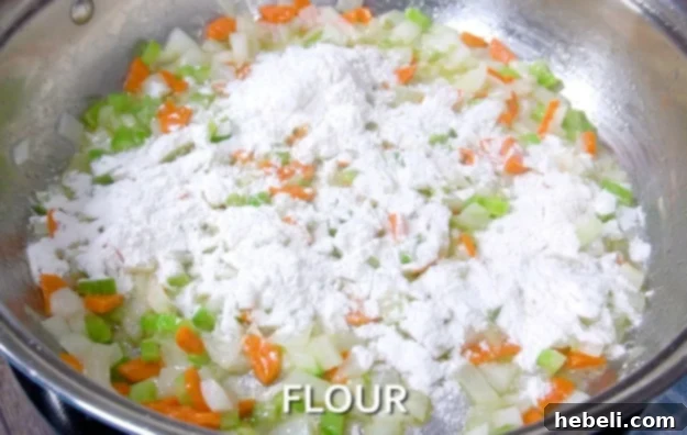 Adding the flour to the sautéed vegetables in a skillet.