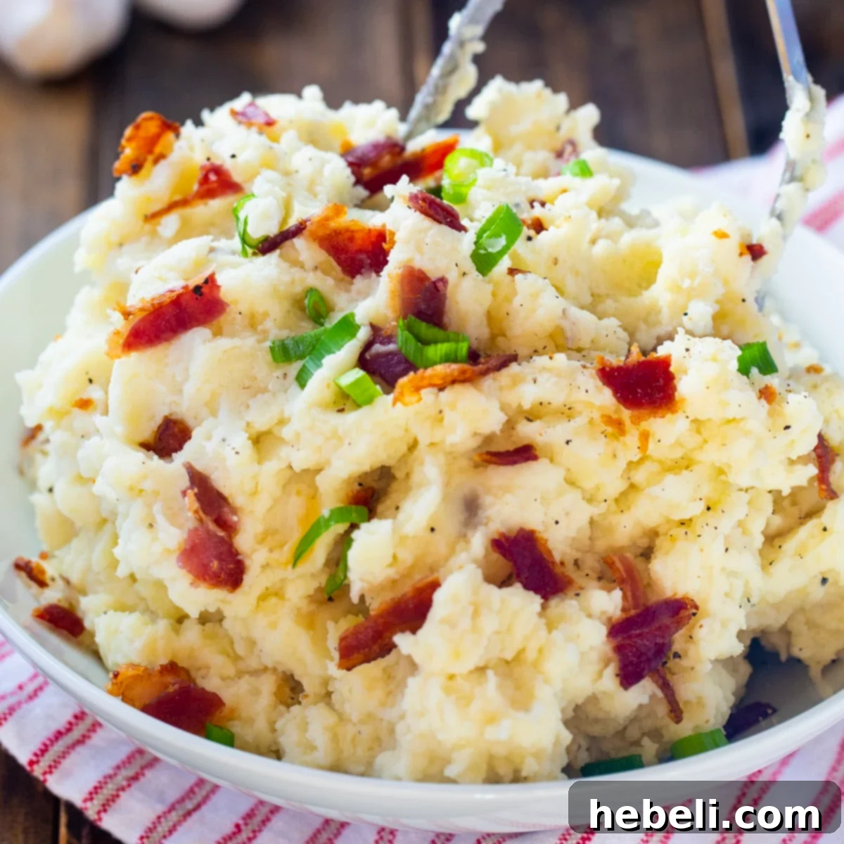 A generous serving bowl filled with Roasted Garlic and Bacon Mashed Potatoes, garnished with crispy bacon bits and fresh green onions.