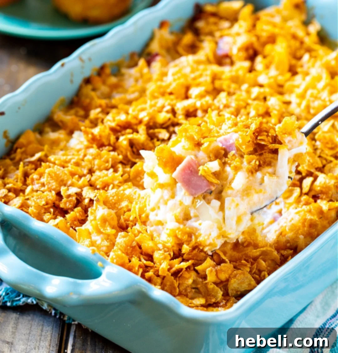 Spoon scooping Funeral Potatoes with Ham out of casserole dish.