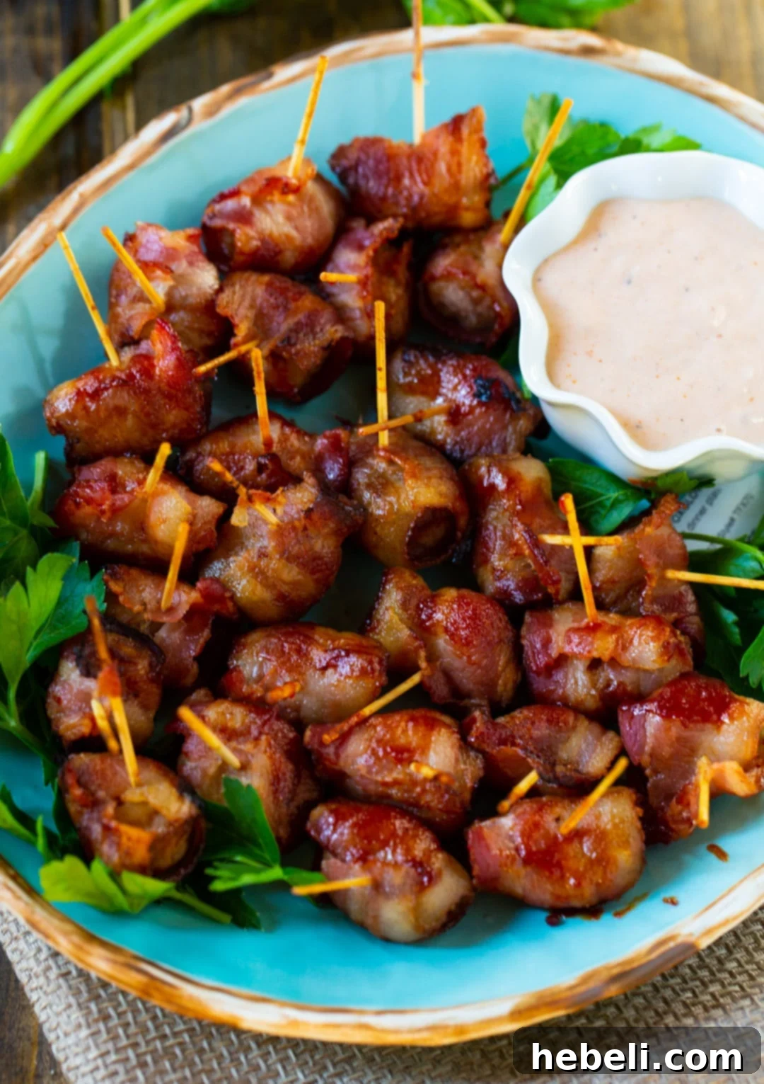 A serving platter brimming with Bacon-Wrapped Water Chestnuts, accompanied by a small bowl of creamy BBQ mayonnaise dipping sauce.