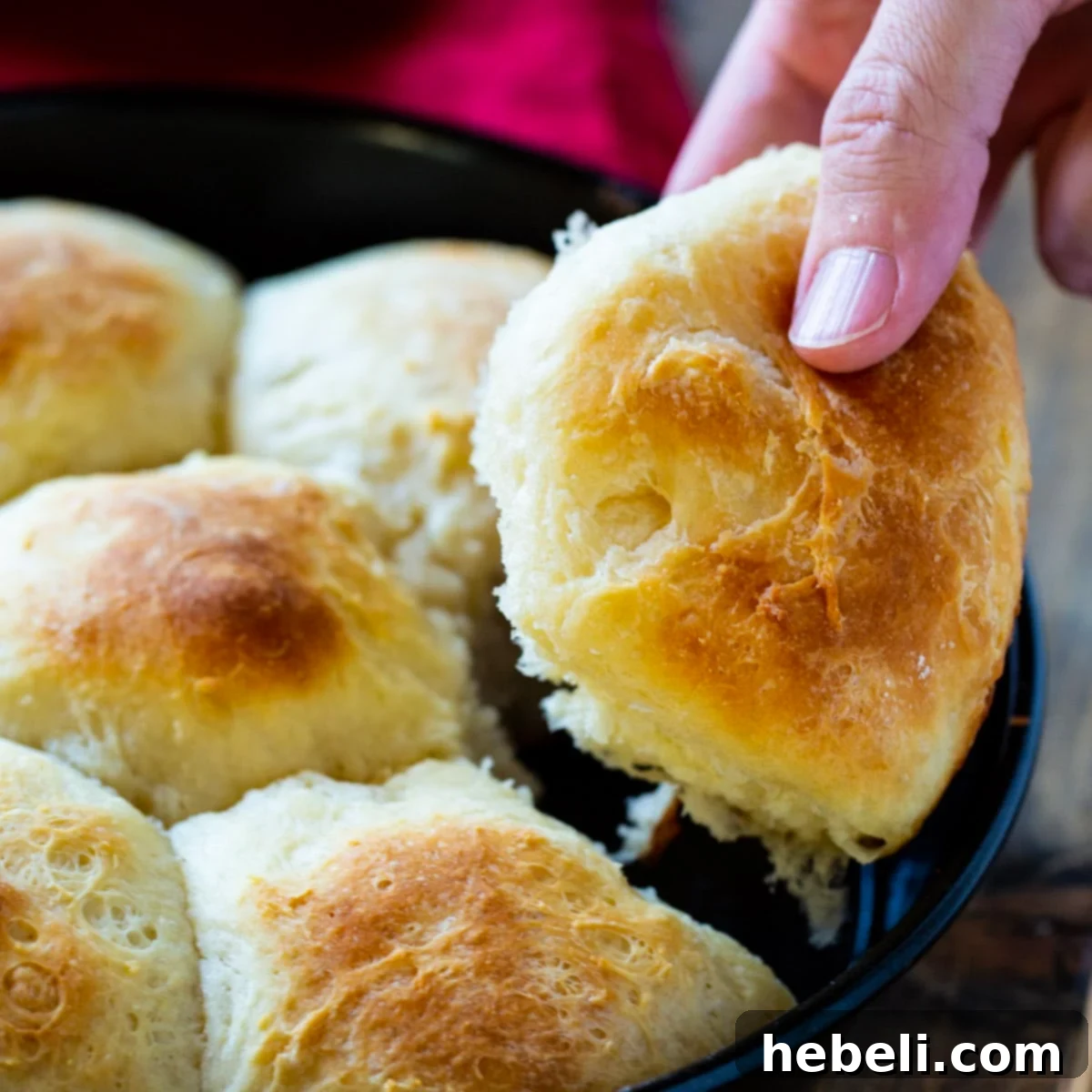 Hand picking up a warm, golden potato roll from a basket.