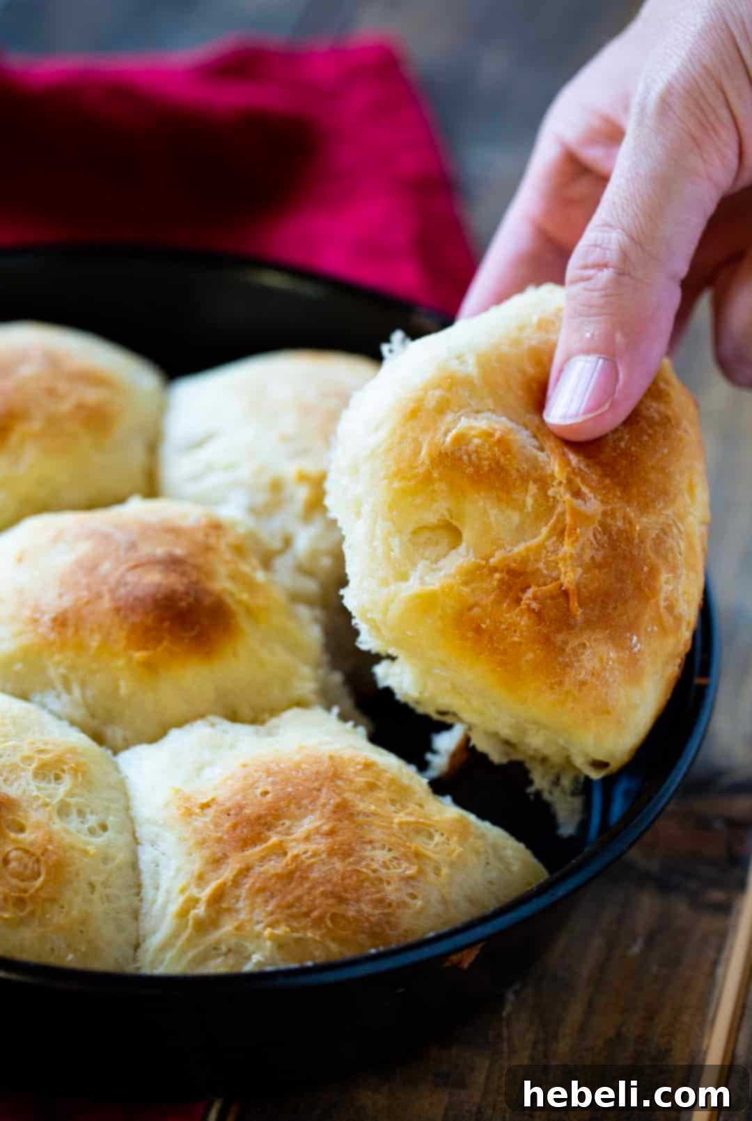 A hand reaching for a golden, fluffy potato roll, showcasing its perfect texture.