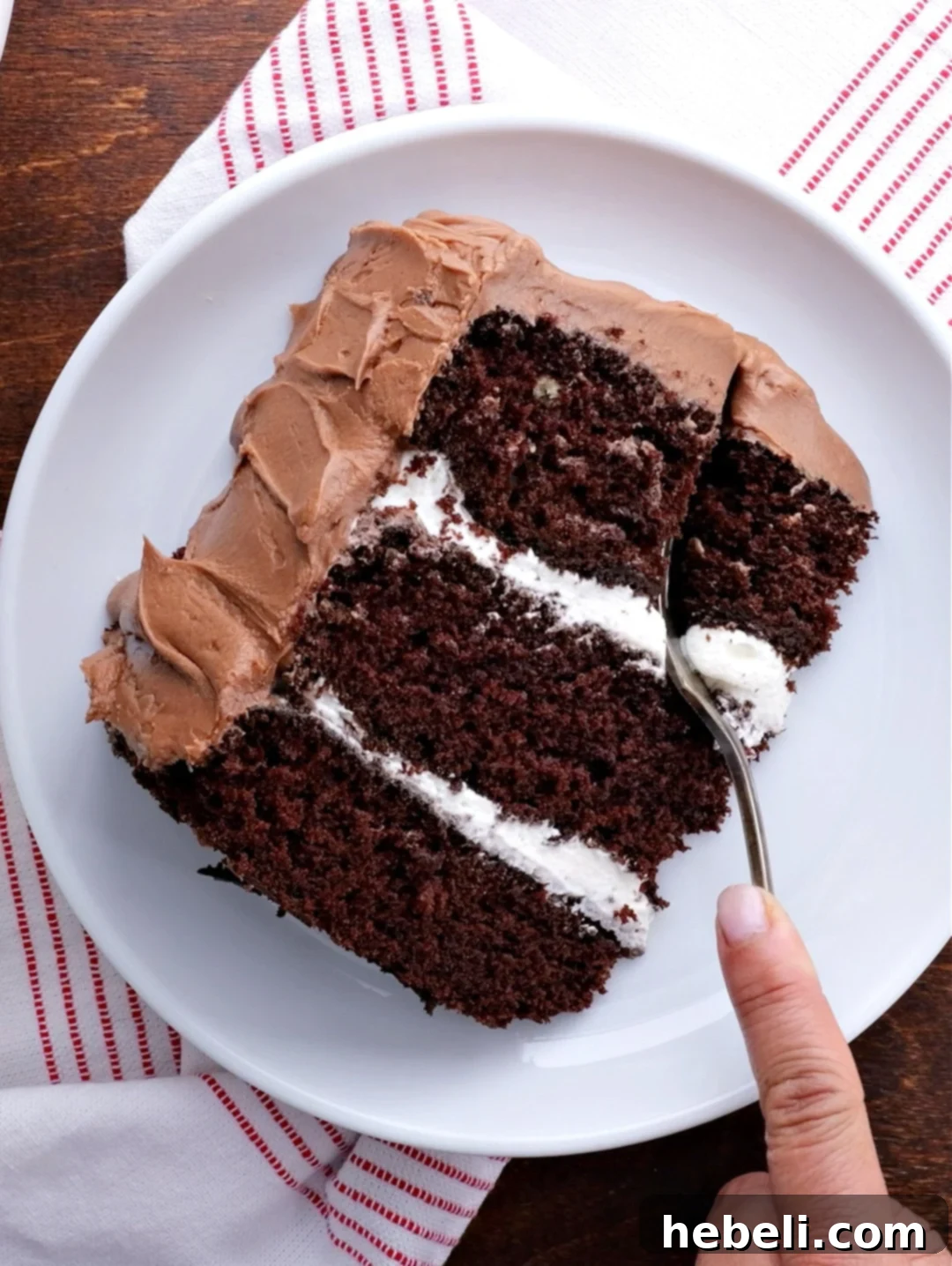 A fork gently cutting into a thick slice of chocolate cake, revealing the distinct layers of moist cake and creamy filling.