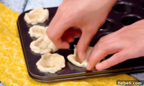 Pressing layers of flaky biscuit dough into mini muffin cups.