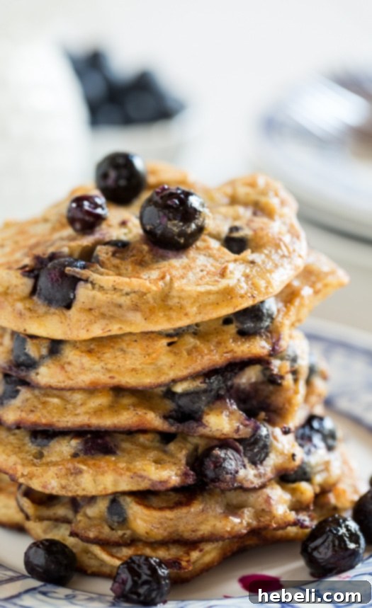 A stack of golden brown Blueberry Almond Protein Pancakes with a light drizzle of maple syrup