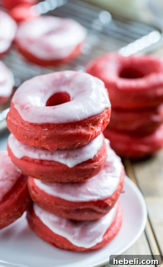 Decadent Red Velvet Glazed Doughnuts 5 A charming plate showcasing Red Velvet Donuts, some partially dipped in glaze, tempting with their rich color and appealing texture.