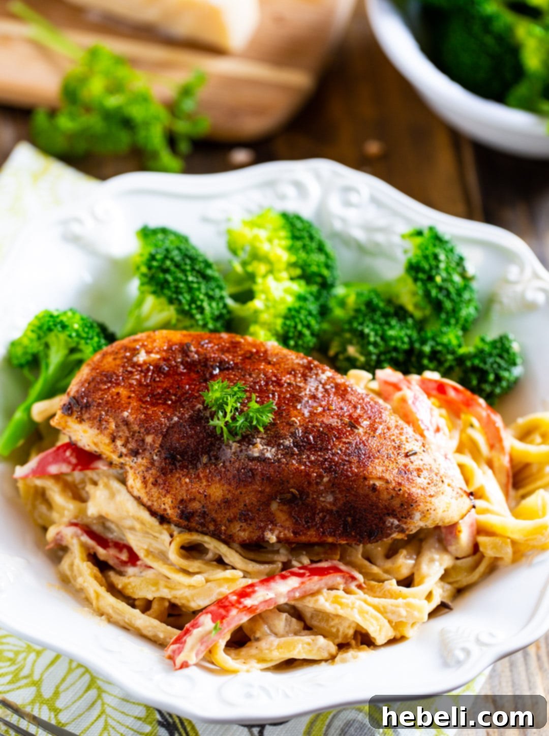 Close-up of Blackened Chicken Fettuccine in a bowl, served alongside fresh steamed broccoli.